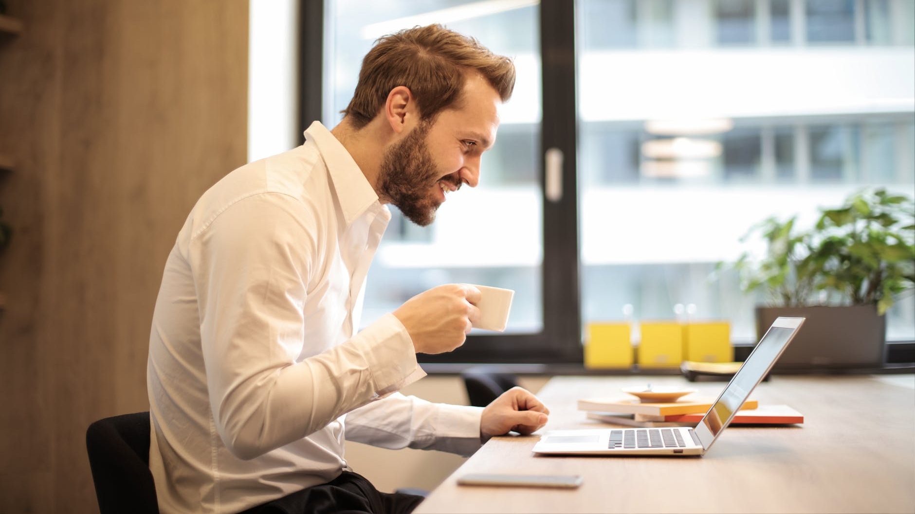 man holding teacup infront of laptop on top of table inside the room